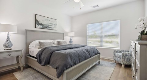 A bedroom with a large bed, a nightstand with a lamp, a chair, and a painting on the wall.