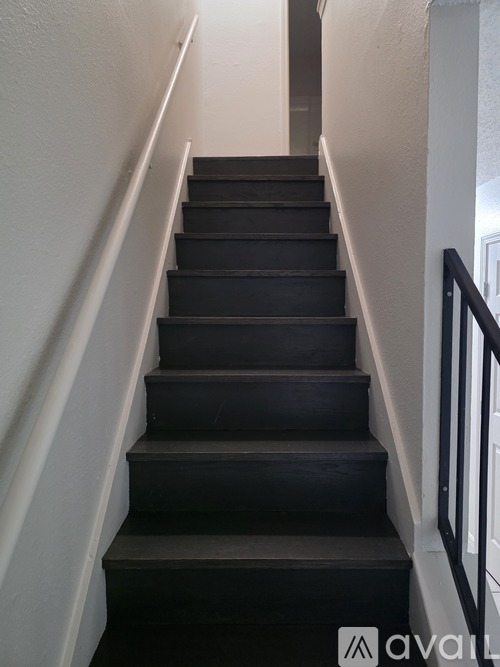 A set of stairs with a black carpeted runner and white walls.