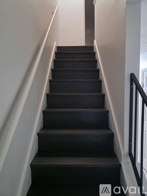A set of stairs with a black carpeted runner and white walls.
