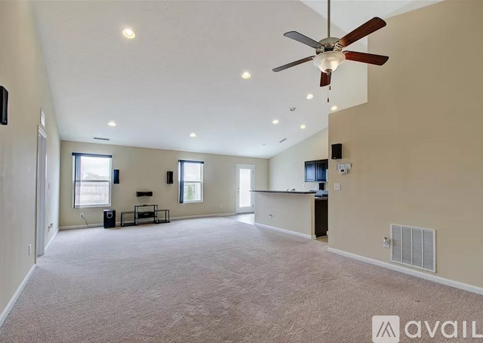 A spacious living room with a ceiling fan and carpeted floor.