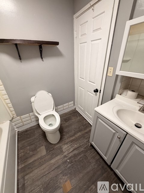 A white toilet in a bathroom with a wooden shelf above it.