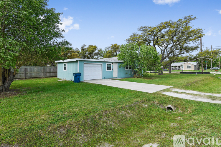 A blue house with a white garage door is surrounded by a green lawn and trees.