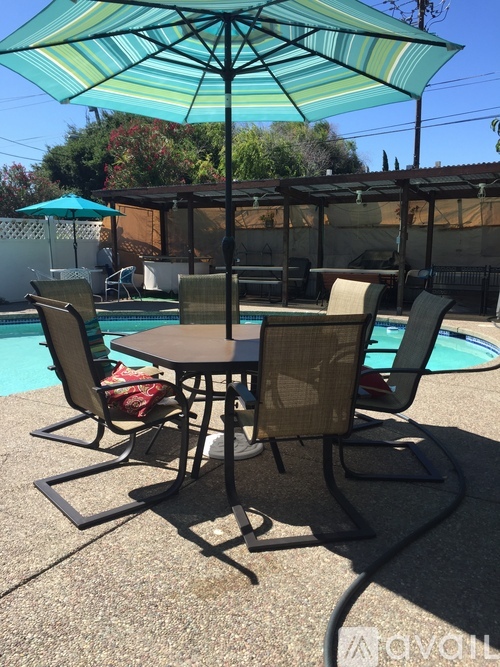 A table with chairs and an umbrella is in the foreground of a pool.