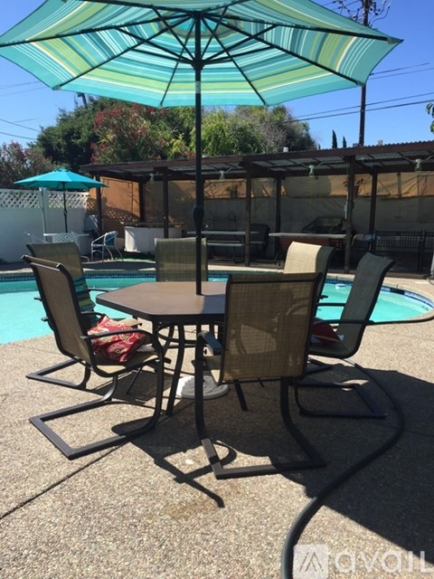 A table with chairs and an umbrella is in the foreground of a pool.