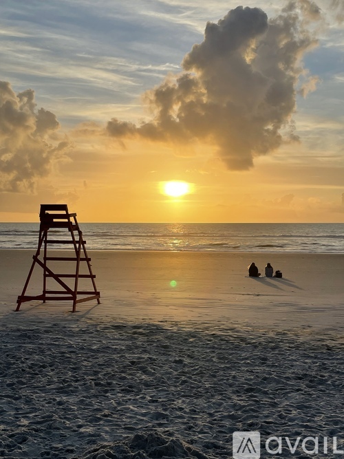 Two people are sitting on the beach near a lifeguard tower as the sun sets.