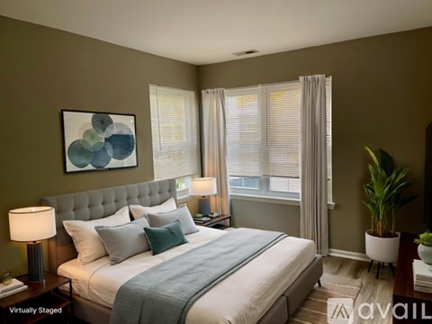 A bedroom with a large bed, a lamp, a potted plant, and a painting on the wall.