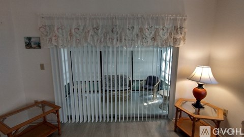 A living room with a couch, a chair, a table with a lamp and a window with curtains.