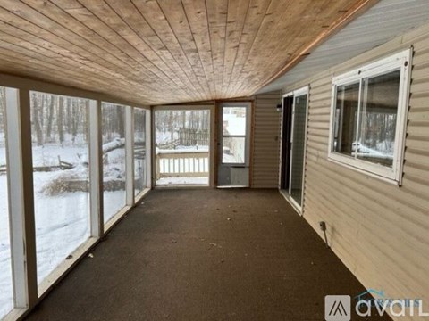 A sunroom with a wooden ceiling and floor, large windows, and a view of a snowy landscape outside.
