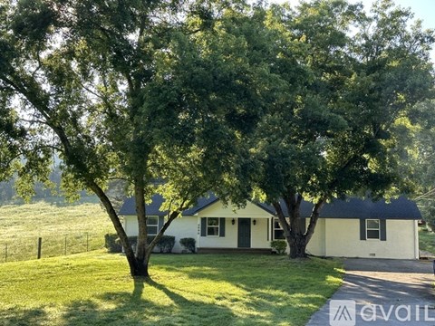 A white house with a black roof is surrounded by green trees.