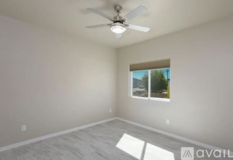 A room with a ceiling fan and a window overlooking a tree.