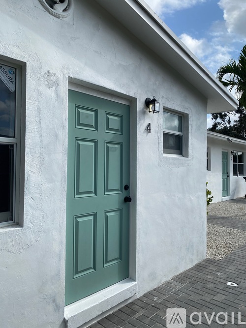 A white house with a green door and a window with a lamp on the wall.