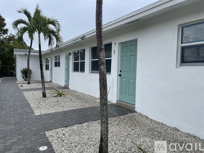 A white house with a green door and a palm tree in front.