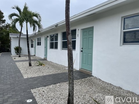 A white house with a green door and a palm tree in front.
