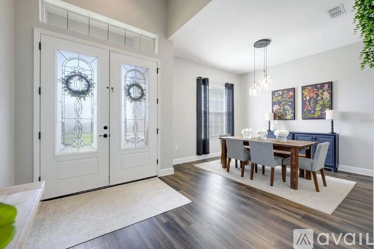 A dining room with a wooden table and chairs, a chandelier, and a view of a kitchen through a glass door.