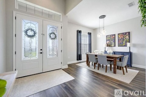 A dining room with a wooden table and chairs, a chandelier, and a view of a kitchen through a glass door.