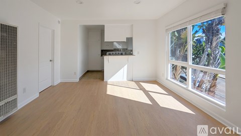 A room with wooden flooring and a large window with a view of trees outside.