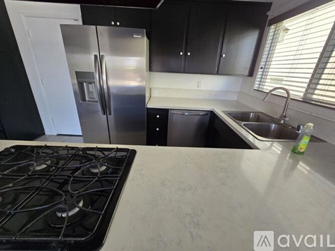 A kitchen with a stove top oven, sink, and black cabinets.