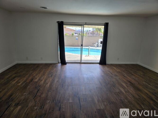 A room with wooden flooring and a sliding glass door leading to a pool.