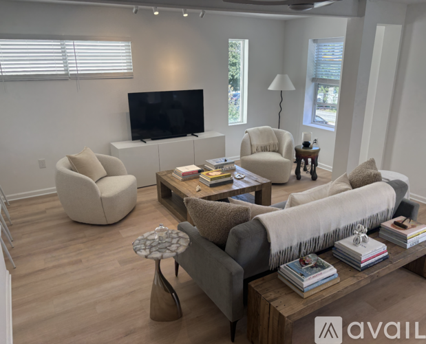 A living room with a grey couch, a white chair, a white ottoman, a wooden coffee table, and a flat screen TV.
