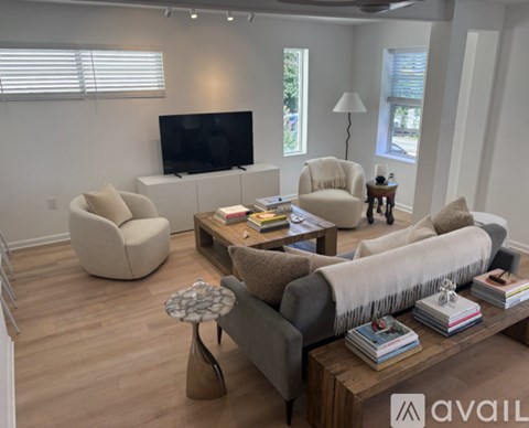 A living room with a grey couch, a white chair, a white ottoman, a wooden coffee table, and a flat screen TV.