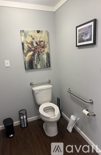 A bathroom with a toilet, trash can, and a painting on the wall.