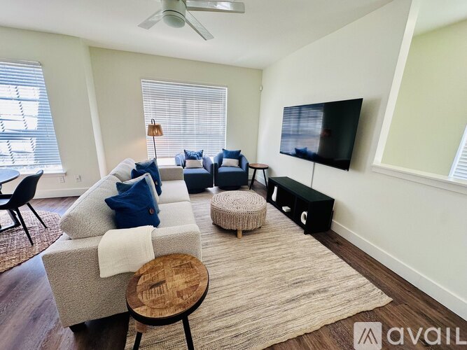 A living room with a grey couch, a wooden stool, and a television on the wall.