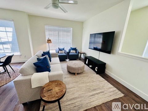A living room with a grey couch, a wooden stool, and a television on the wall.