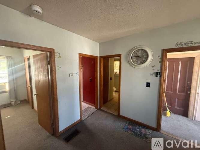 A room with a clock on the wall and a broom in the corner.