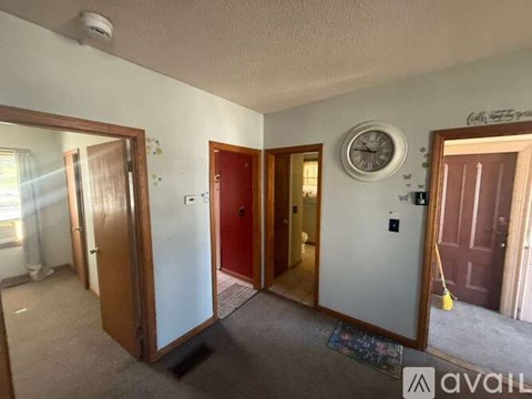 A room with a clock on the wall and a broom in the corner.