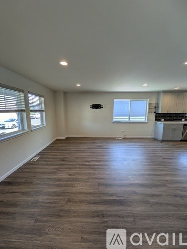 A spacious room with wooden flooring and a window with blinds.