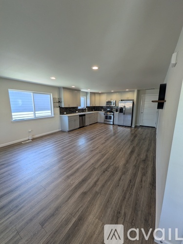 A spacious room with wooden flooring and a kitchen area in the background.