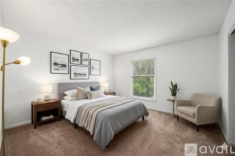 A bedroom with a bed, nightstand, lamp, chair, and pictures on the wall.
