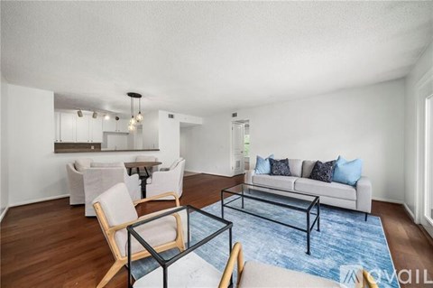 A modern living room with a white couch, a glass coffee table, and a dining table with chairs.