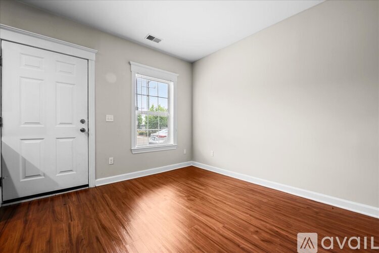 A room with a white door and a window with a view of trees and a house.