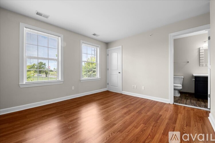 A spacious room with wooden floors and a window overlooking a green area.