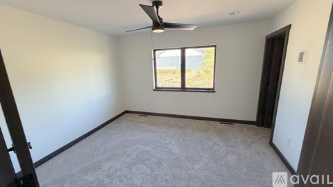 A room with a ceiling fan and a window showing a view of a fence and trees.