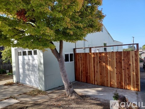A tree is in front of a white garage and a wooden fence.