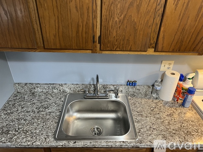 A kitchen sink with a granite countertop and wooden cabinets.