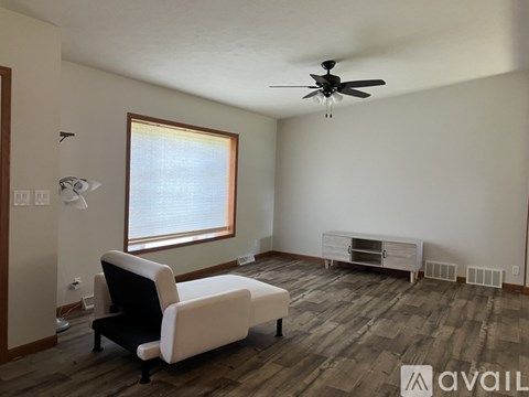 A living room with a black and white chair, a ceiling fan, and a window with blinds.
