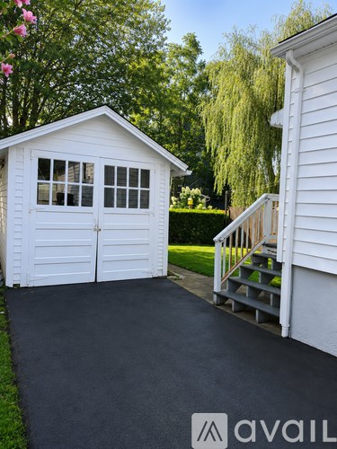 A white garage with a black driveway and a white house in the background.