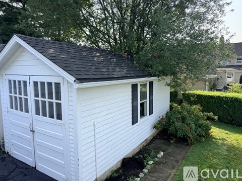 A small white shed with a black roof and a wooden fence.