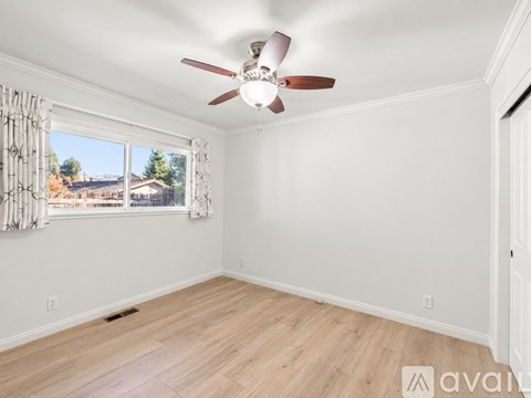 A room with a ceiling fan and a window with a view of a fence and trees.