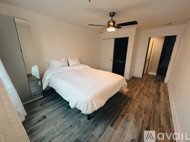 A bedroom with a bed, a ceiling fan, and a wooden floor.