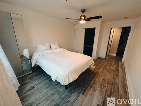 A bedroom with a bed, a ceiling fan, and a wooden floor.