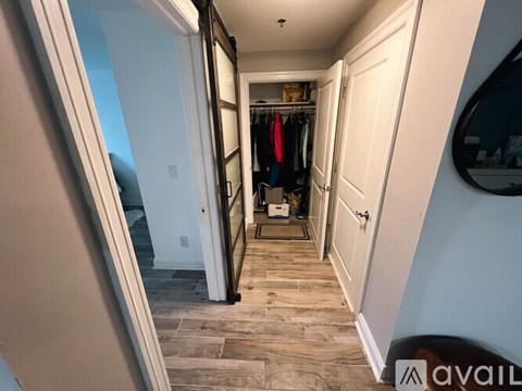 A hallway with a mirror on the wall and a closet with clothes hanging.