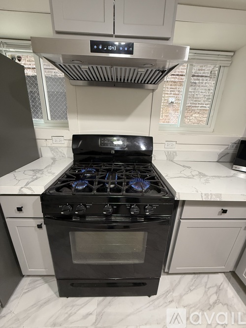 A black stove top oven with blue knobs is in a kitchen with white cabinets.