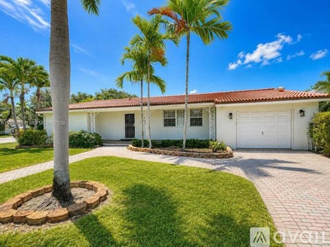 A house with a red tile roof and white walls is surrounded by palm trees.