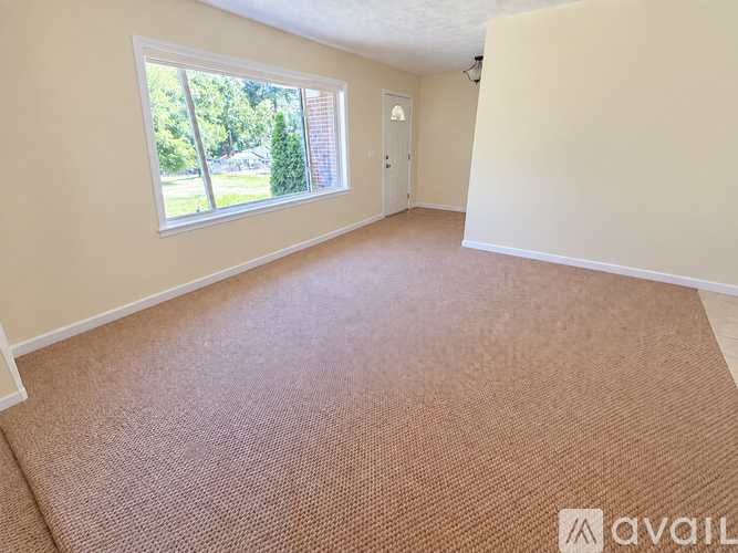 A room with a carpeted floor and a window overlooking a yard.