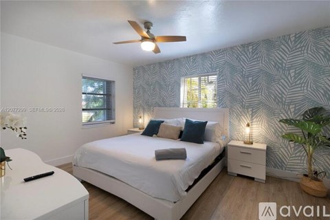 A bedroom with a white bed, a ceiling fan, and a wallpapered wall.