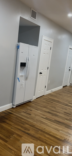 A white fridge with a blue handle is in a room with wooden floors and white walls.
